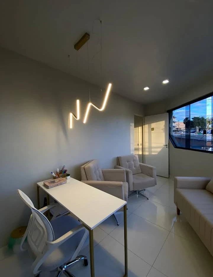 Consultório da Clínica Alvo com mesa, poltronas claras, luminária pendente e janela ampla