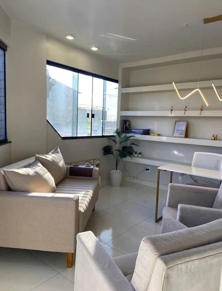 Sala de atendimento da Clínica Alvo com sofá e poltronas claras, estante iluminada e luz natural